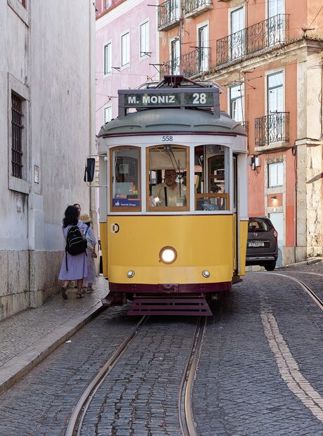 Żółty tramwaj linii 28 na wąskiej uliczce w Lizbonie